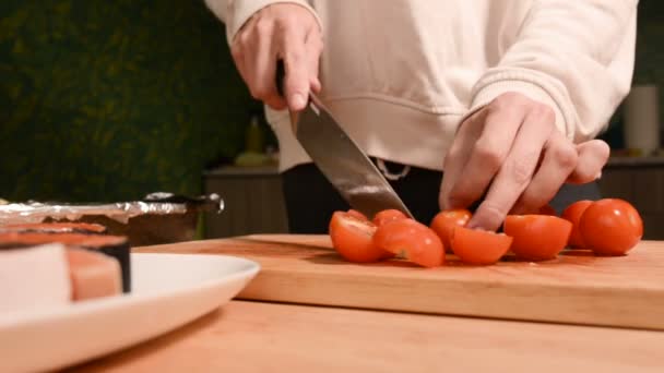 Primer plano de las niñas manos en la cocina de casa en una tabla de cortar madera cuchillos pequeños tomates cherry con un cuchillo. Cocina casera — Vídeos de Stock