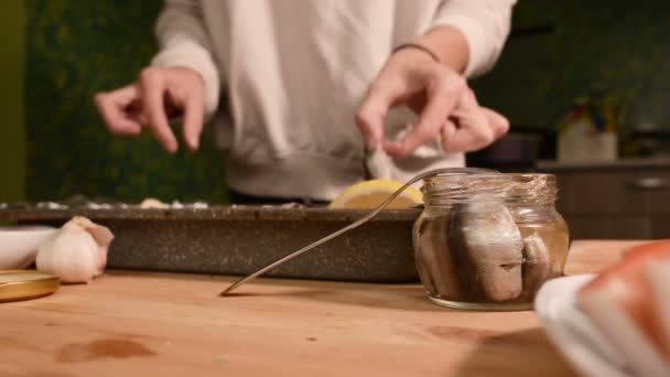 Close-up van handen van een meisje op de binnenlandse keuken legt sprot uit een glazen pot op een dienblad met een schotel. Gezond thuis koken — Stockvideo