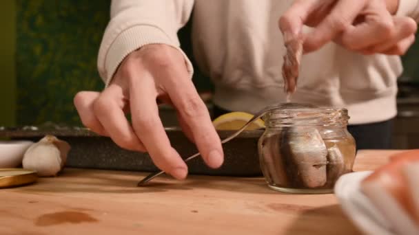 El primer plano de las manos de una muchacha en la cocina de casa pone espadines de un frasco de cristal en una bandeja con un plato. Cocina casera saludable — Vídeos de Stock