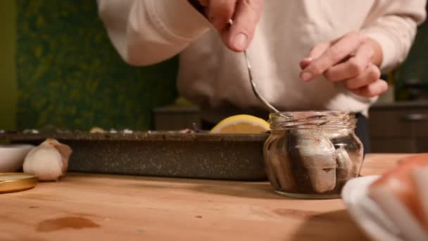 Close-up van handen van een meisje op de binnenlandse keuken legt sprot uit een glazen pot op een dienblad met een schotel. Gezond thuis koken — Stockvideo