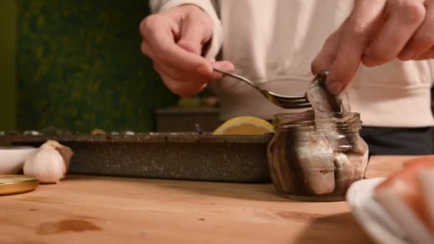 El primer plano de las manos de una muchacha en la cocina de casa pone espadines de un frasco de cristal en una bandeja con un plato. Cocina casera saludable — Vídeos de Stock