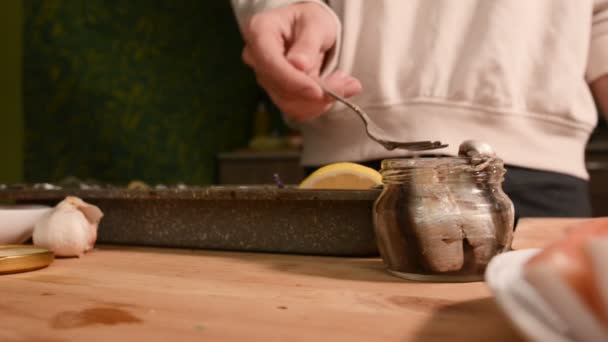 Крупным планом руки девушки на домашней кухне выкладывают шпроты из стеклянной банки на поднос с тарелкой. Здоровое домашнее питание — стоковое видео