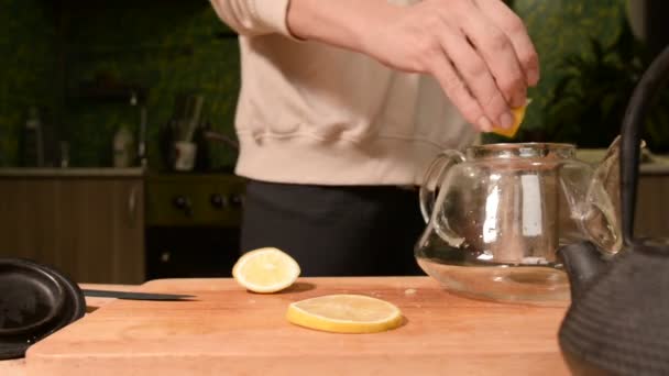 Close-up de mãos femininas estão cortando uma faca com limões em pedaços e espremendo para fazer chá em uma mesa de madeira de cozinha caseira. Casa chá de cozinha — Vídeo de Stock