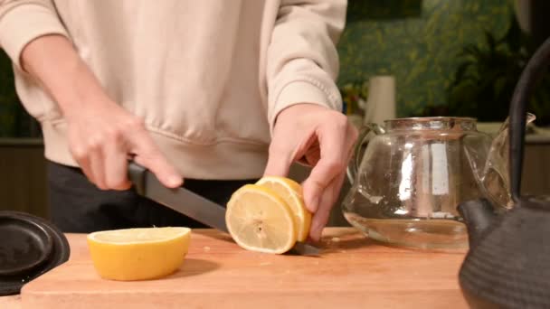 Close-up de mãos femininas estão cortando uma faca com limões em pedaços e espremendo para fazer chá em uma mesa de madeira de cozinha caseira. Casa chá de cozinha — Vídeo de Stock