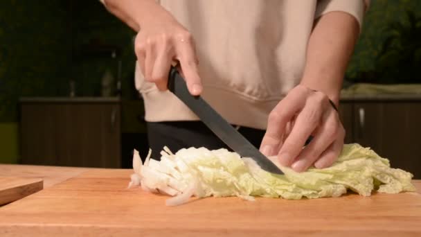 Крупним планом руки дівчини на домашній кухні на дерев'яній обробній дошці ножі Пікінська капуста для салату. Домашня кухня — стокове відео