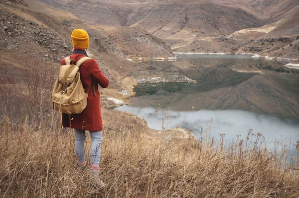 Ett porträtt från baksidan av en flicka resenär på bakgrund av en sjö i fjällen på hösten eller tidigt på våren. Resor-konceptet — Stockfoto