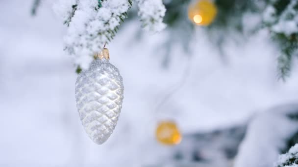 Close-up of a Christmas toy on a snow-covered lively tree in the winter forest on the background of lights. Small DOF — Stock Video