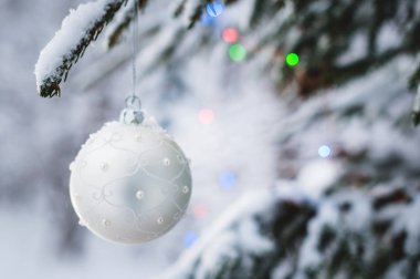 Kış ormanındaki karla kaplı bir ağaçta, ışıkların arkasındaki bir Noel oyuncağının yakın çekimi.