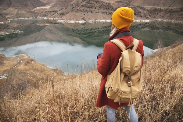 Um retrato da parte de trás de uma fotógrafa viajante no fundo de um lago nas montanhas no outono ou início da primavera. Conceito de viagem — Fotografia de Stock