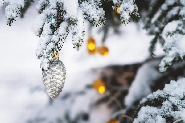 Close-up of a Christmas toy on a snow-covered lively tree in the winter forest on the background of lights — Stock Photo, Image