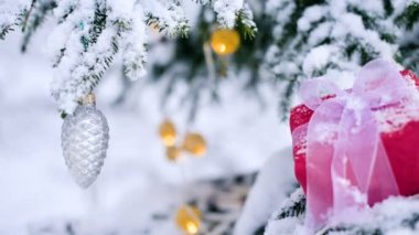 Yakın çekim kırmızı yeni yıl hediye yanındaki Noel oyuncaklar kış orman içinde karla kaplı Noel ağaç dalları üzerinde beyaz bir kurdele ile. Hediyeler Noel ve yeni yıl kavramı