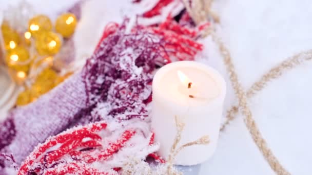 Um close-up de um ursinho de pelúcia com velas de Natal em um acolhedor xadrez xadrez ao ar livre ao lado de uma caixa de presente vermelha polvilhada com neve. Natal clima festivo — Vídeo de Stock