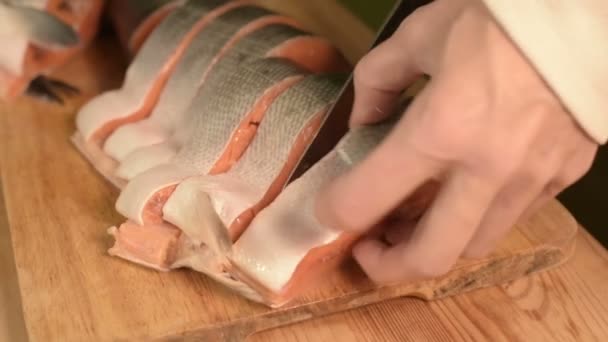 Κοντινό πλάνο γυναικεία χέρια κόβοντας με μαχαίρι έναν μεγάλο σολομό σε ένα ξύλινο τραπέζι μαγείρεμα στο σπίτι — Αρχείο Βίντεο