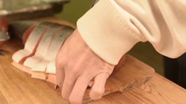 Close-up de mãos femininas estão cortando com uma faca um grande salmão em uma mesa de madeira de cozinha caseira — Vídeo de Stock