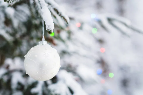 Close-up de um brinquedo de Natal em uma árvore animada coberta de neve na floresta de inverno no fundo das luzes — Fotografia de Stock