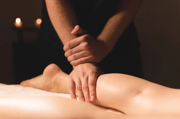 Close-up van mannelijke handen doen kalf massage van vrouwelijke benen in een donkere kamer met kaarsen op de achtergrond. Cosmetologie en wellness-behandelingen — Stockfoto