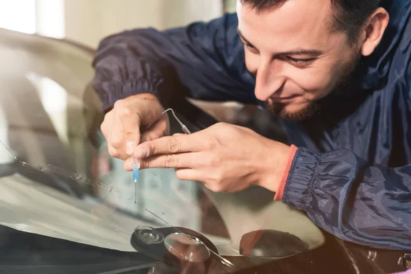 Il primo piano di un riparatore di parabrezza professionale riempie una fessura del vetro con uno speciale polimero attraverso una siringa. Eliminazione di crepe e schegge sui parabrezza — Foto Stock