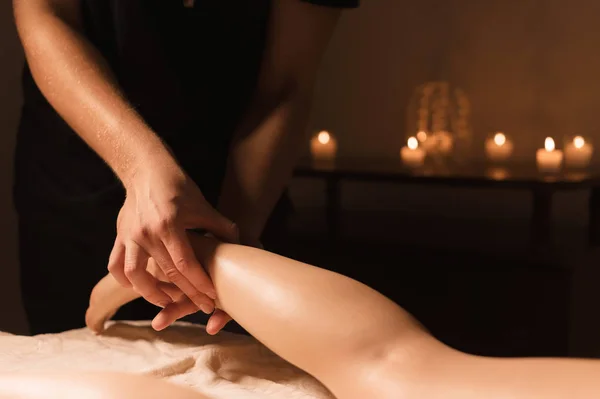 男性手的特写在黑暗的房间里做小腿按摩女性腿在背景蜡烛 美容和水疗护理 — 图库照片