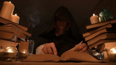 Mum ışığı ve seyir için bir kitap üzerinde bir büyü tarafından karanlık bir odada bir başlıklı orta yakın çekim kız sihirbaz. Düşük anahtar. Mistik küçük Dof