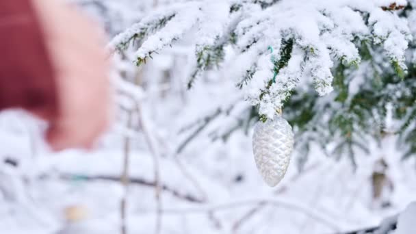 근접 여성 손 장갑 손 새 해 나무의 눈 덮인 지점에서 진짜 겨울에 크리스마스 장난감 장식 트리를 달아 — 비디오