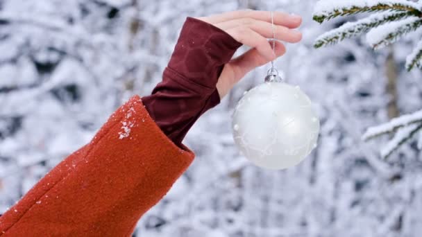 Close-up weibliche Hände in Fäustlingen Hände hängen Weihnachtsspielzeug Dekorationsbaum in einem echten Winter von einem schneebedeckten Zweig eines Neujahrsbaums — Stockvideo