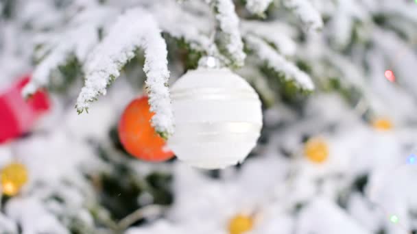 Primo piano di un giocattolo di Natale su un albero vivace coperto di neve nella foresta invernale sullo sfondo di luci. Piccolo DOF — Video Stock