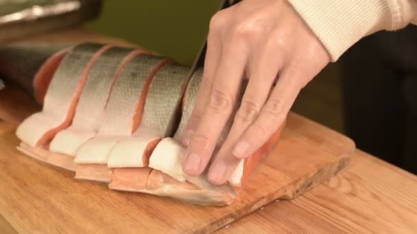 Close-up de mãos femininas estão cortando com uma faca um grande salmão em uma mesa de madeira de cozinha caseira — Vídeo de Stock