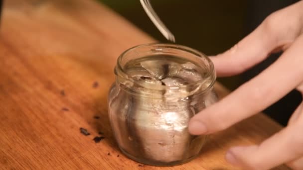 El primer plano de las manos de una muchacha en la cocina de casa pone espadines de un frasco de cristal en una bandeja con un plato. Cocina casera saludable — Vídeo de stock