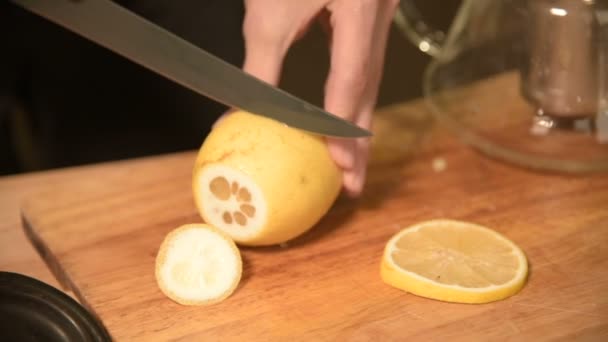 Close-up de mãos femininas estão cortando uma faca com limões em pedaços e espremendo para fazer chá em uma mesa de madeira de cozinha caseira. Casa chá de cozinha — Vídeo de Stock