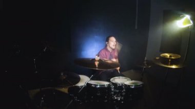 Uzun saçlı davulcular davul kiti karanlık bir odada bir siyah arka plan üzerinde oynamak. Rock müzisyeni. Statik plan. Geniş açı