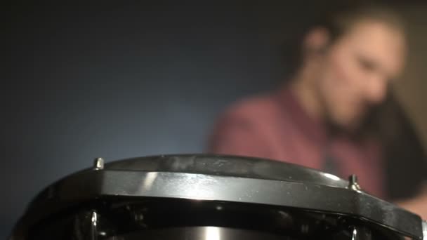 Los bateristas de pelo largo tocan el kit de batería en una habitación oscura sobre un fondo negro. Músico de rock. Plan estático. Ángulo ancho — Vídeos de Stock