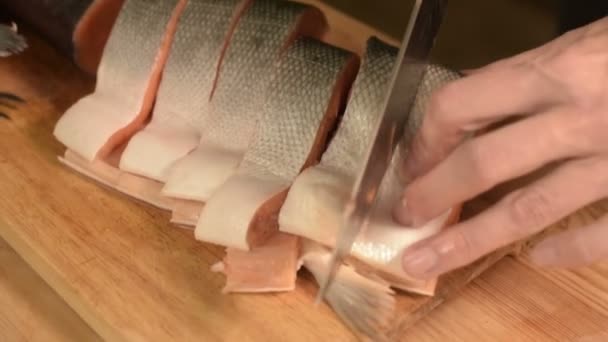 Gros plan des mains des femmes coupent avec un couteau un gros saumon sur une table en bois de cuisine maison — Video