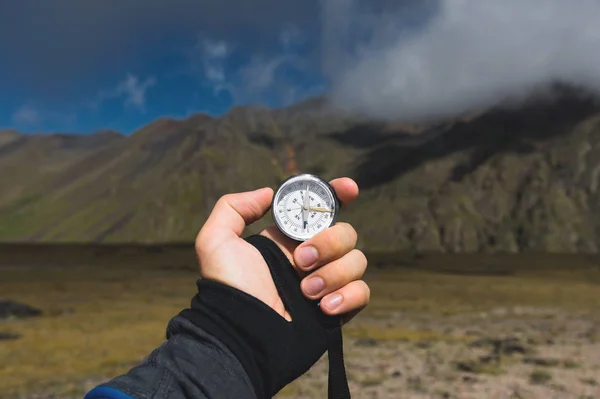 Viewpoint shot. A first-person view of a mans hand holds a compass against the background of an epic landscape with cliffs hills and a blue sky with clouds