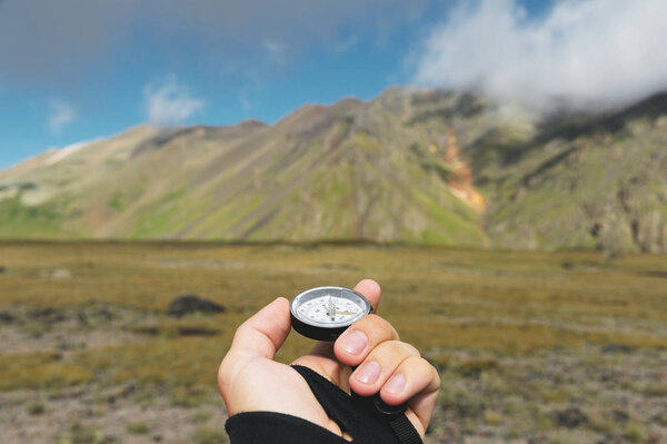 Снимок со смотровой. Вид от первого лица руки человека держит компас на фоне эпического ландшафта с скалами холмов и голубое небо с облаками
