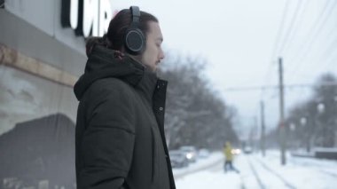 Kışın bir tramvay durağında duran ve müzik bir tramvay için bekleyen Kulaklığımda sakallı genç bir uzun saçlı adam portresi