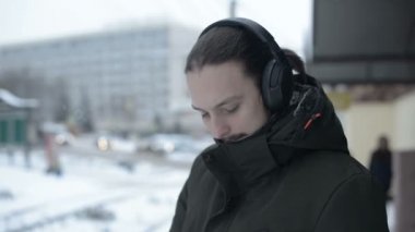 Kışın bir tramvay durağında duran ve müzik bir tramvay için bekleyen Kulaklığımda sakallı genç bir uzun saçlı adam portresi