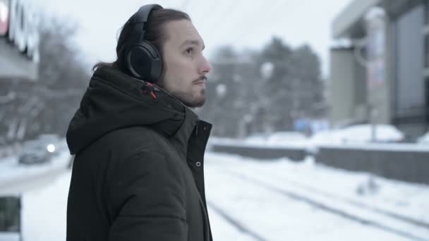 Portret Młodego Mężczyzny Długowłosy Brodą Słuchawkach Stojąc Przystanku Zimie Czekając — Wideo stockowe
