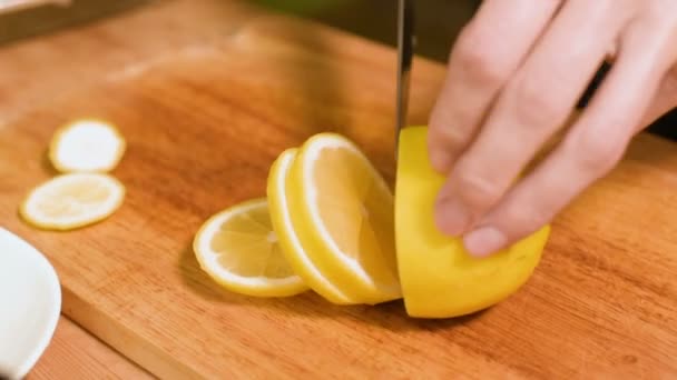 Closeup ev mutfak ahşap kesme tahtası üzerinde bir kıza el. Sarı limon gezginci üzerinde keser. Ev yemekleri — Stok video