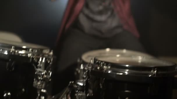 Los bateristas de pelo largo tocan el kit de batería en una habitación oscura sobre un fondo negro. Músico de rock. Plan estático. Ángulo ancho — Vídeo de stock