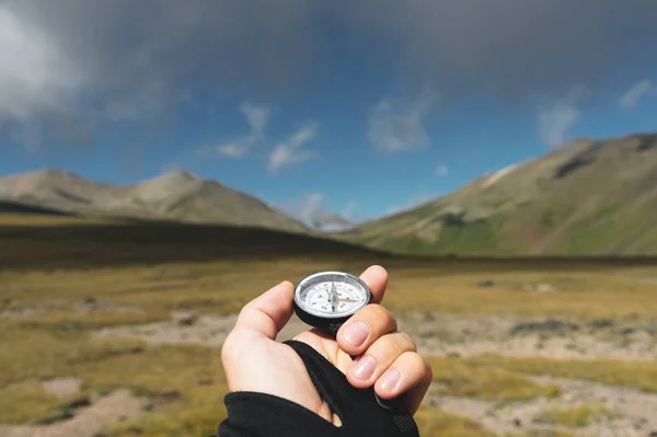 Viewpoint shot. A first-person view of a mans hand holds a compass against the background of an epic landscape with cliffs hills and a blue sky with clouds