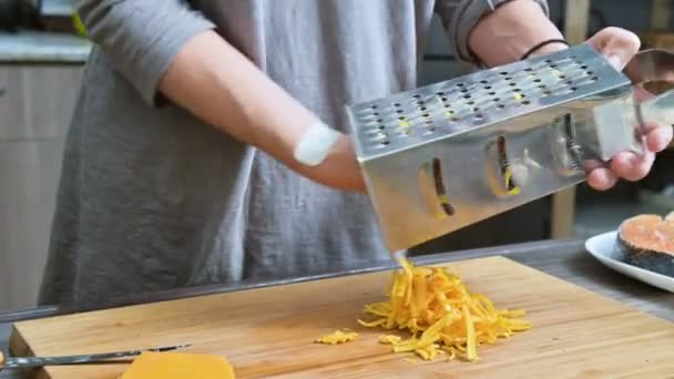 Close-up de mãos femininas esfregando queijo em um ralador de metal. Cozinhar na cozinha da casa — Vídeo de Stock