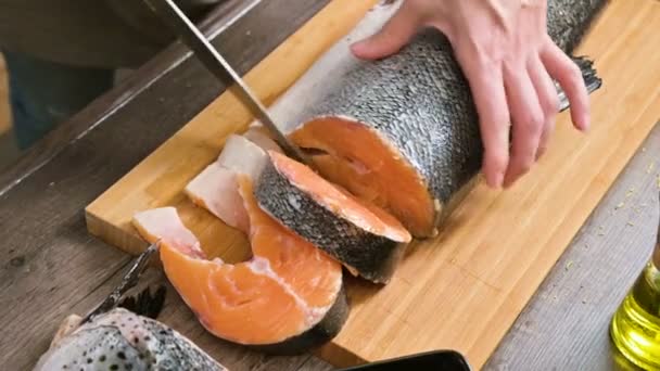 Primer plano de las manos femeninas están cortando con un cuchillo un salmón grande en una mesa de madera de cocina casera — Vídeo de stock