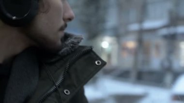 Bir ceket portre genç uzun saçlı sakallı adam kapatın ve büyük kulaklıklar pencerenin tramvayla toplu taşıma oturur ve müzik veya bir sesli kitap için kışın dinler