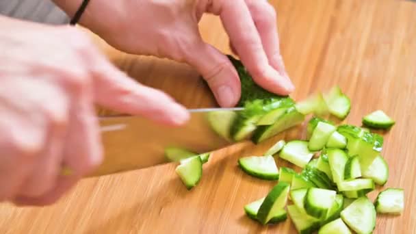 Fechar-se de umas mãos femininas que cortam uma faca de pepino para cozinhar a salada em uma tábua de redução de madeira. Cozinha caseira. Alimentos saudáveis — Vídeo de Stock