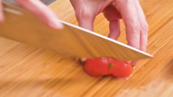 El primer plano de las manos femeninas con un cuchillo está cortando tomates para hacer ensalada en una tabla de cortar de madera. Cocina casera. Alimento saludable — Vídeos de Stock