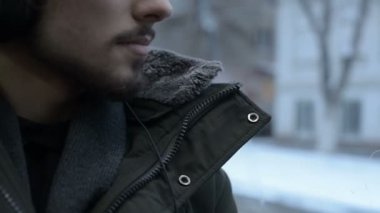Bir ceket portre genç uzun saçlı sakallı adam kapatın ve büyük kulaklıklar pencerenin tramvayla toplu taşıma oturur ve müzik veya bir sesli kitap için kışın dinler