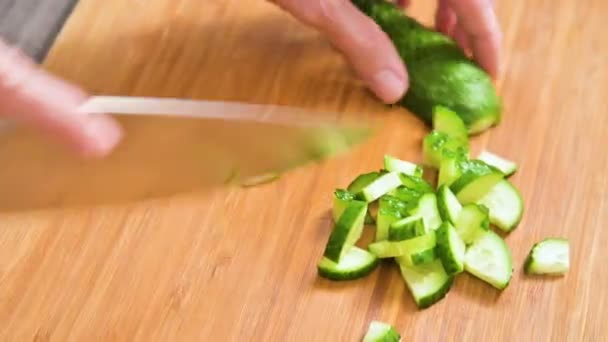 Fechar-se de umas mãos femininas que cortam uma faca de pepino para cozinhar a salada em uma tábua de redução de madeira. Cozinha caseira. Alimentos saudáveis — Vídeo de Stock