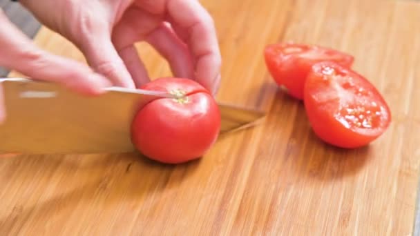 Close-up de mãos femininas com uma faca estão cortando tomates para fazer salada em uma placa de corte de madeira. Cozinha caseira. Alimentos saudáveis — Vídeo de Stock