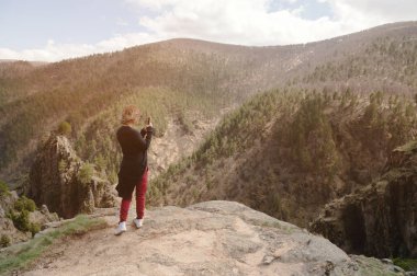 Portre onun Smartphone'da kayalar ile destansı bir manzara fotoğrafını çekmek bir seyahat kız arkadan