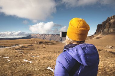 Onun Smartphone'da kayalar ile destansı bir manzara fotoğrafını çekmek bir kap ile aşağı ceket seyahat bir kız arkasından yakın çekim portre